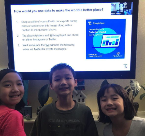 Three smiling kids in front of a slide that says how would you use data to make the world a better place.